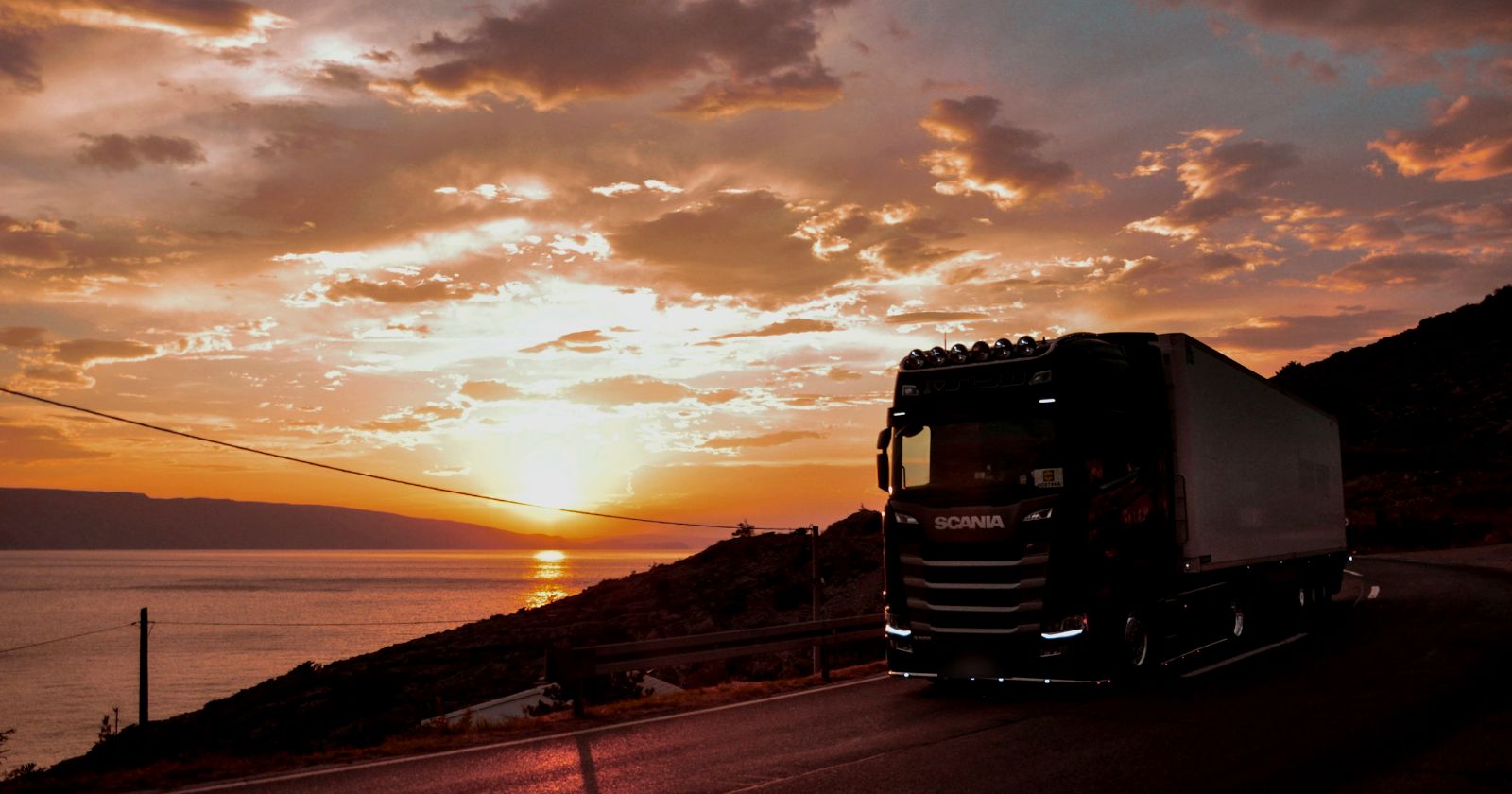 Camión con semirremolque en una ruta de costa al atardecer